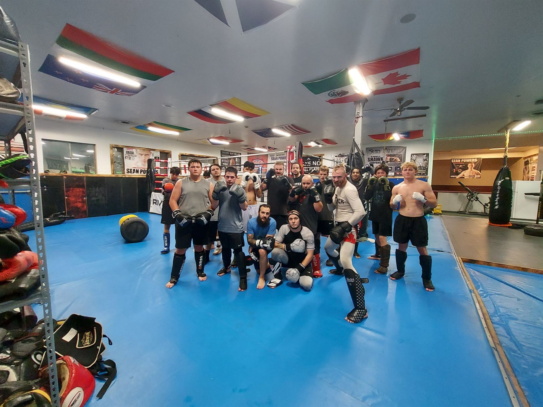 Fighters and coaches posing on the blue mats inside Power MMA